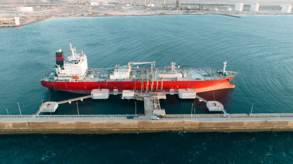 Aerial shot of a red cargo ship docked at an industrial port with clear blue water.